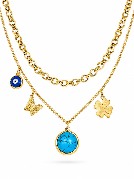 Gold dual-layer charm necklace set with rolo chain and cable chain featuring evil eye, butterfly, turquoise disc, four-leaf clover and rolo ring charms — white background